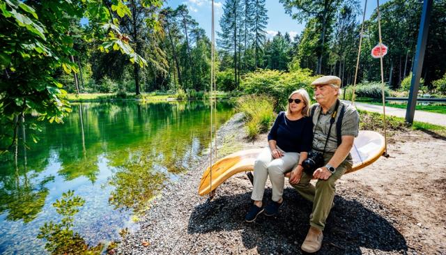 Zwei Senioren sitzen auf einer großen Schaukel am Waldsee